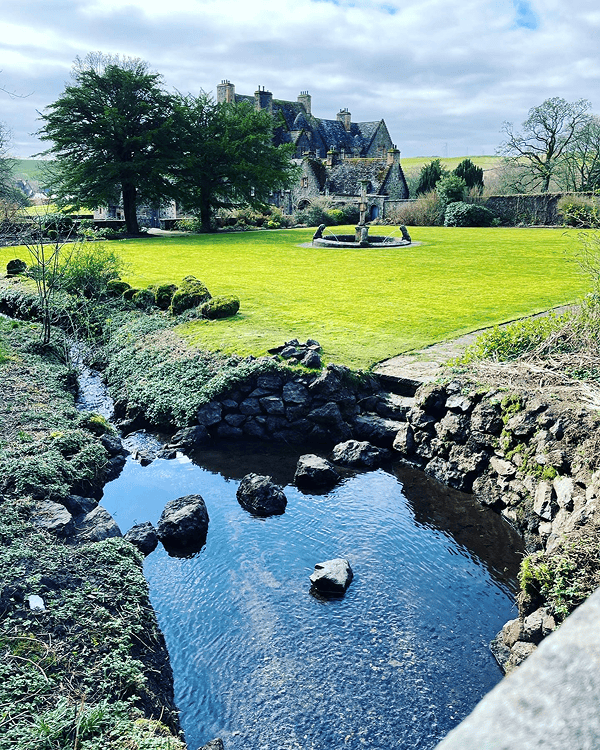  A beautiful stately home front garden with superbly mowed grass and pebble stones around the large front parking area with a 4 by 4 vehicle parked at the corner 