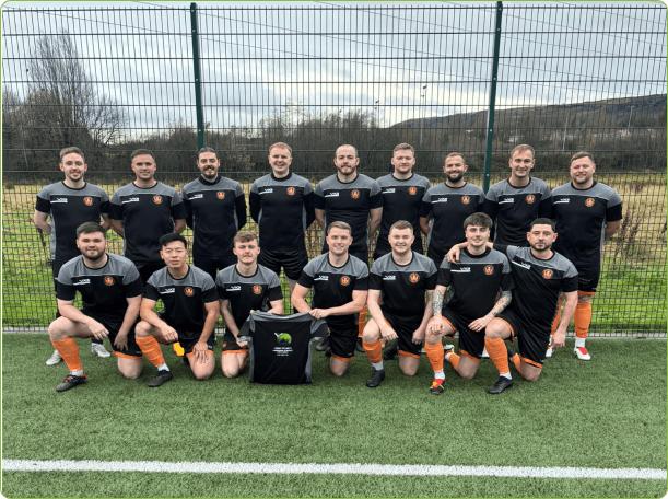 A image of the Glenifer Thistle first team typical football team photo with 2 rows of players.  The first row kneels the second row stands.  In the middle there is a t-shirt with Down To Earth Garden Services sponsoring Glenifer Thistle.