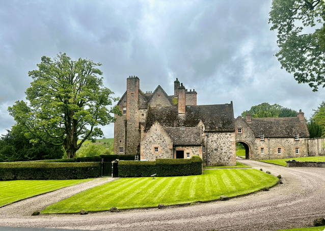 This is a picture of a stately home with beautiful cur grass and gravel stones and trees around the property