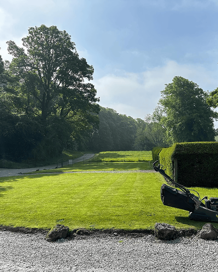 A beautifully mowed grass lawn with stripes in an area that looks like the north of Scotland with an old fashioned cottage building on a hillock on a beautiful summers day with the North Sea in the background